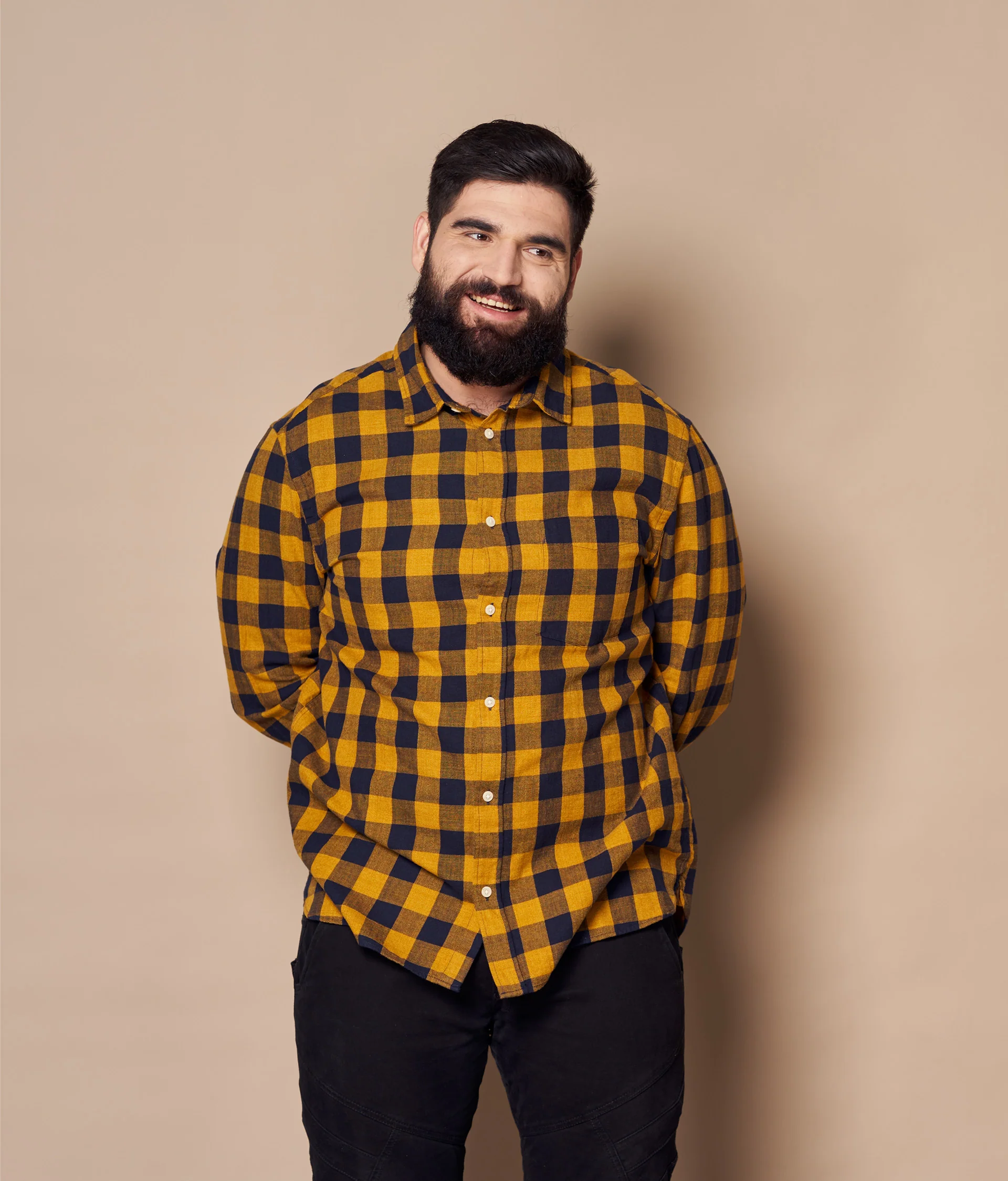 Portrait of a smiling man with a beard wearing a yellow and navy blue plaid shirt.