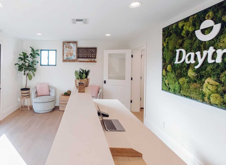 Wellness center reception area with counter, seating, plants, and a large green wall art piece with the Daytryp logo.