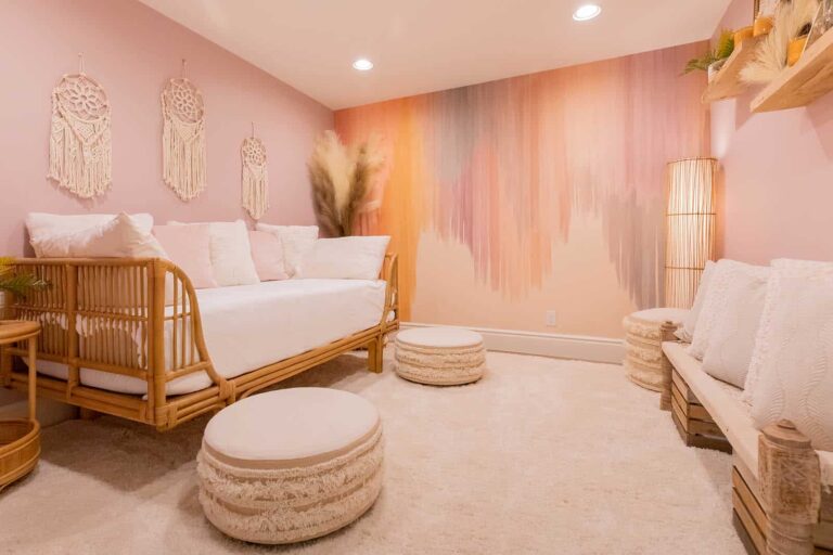A room with a colorful abstract mural on the wall, a wooden daybed, two round ottomans, a bench, and decorative hangings.