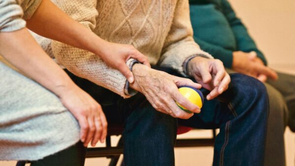 A caregiver gently holding the arm of an elderly person who is holding a colorful stress ball.
