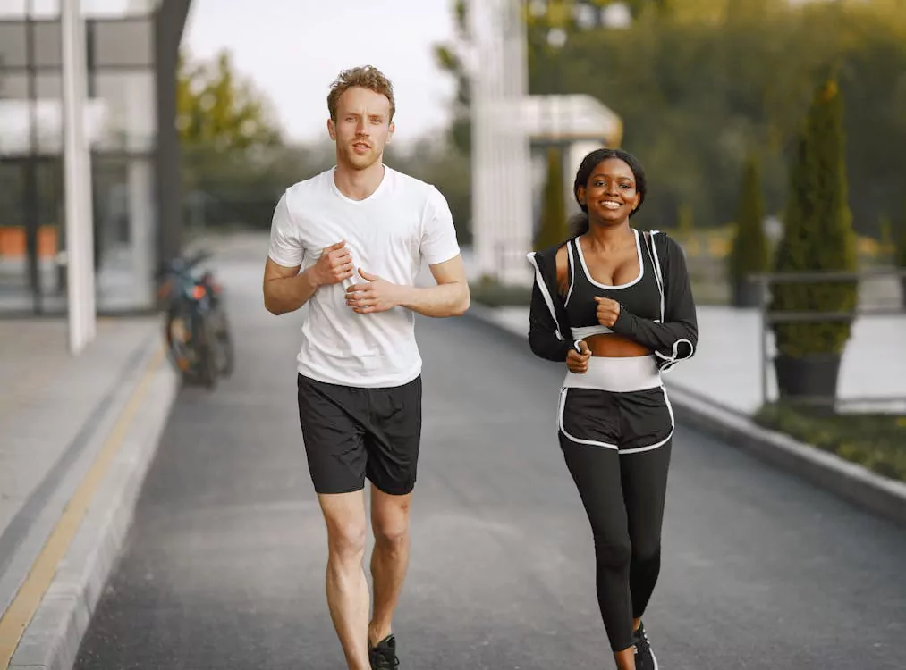 A man and a woman in athletic wear jogging side by side along an outdoor walkway.