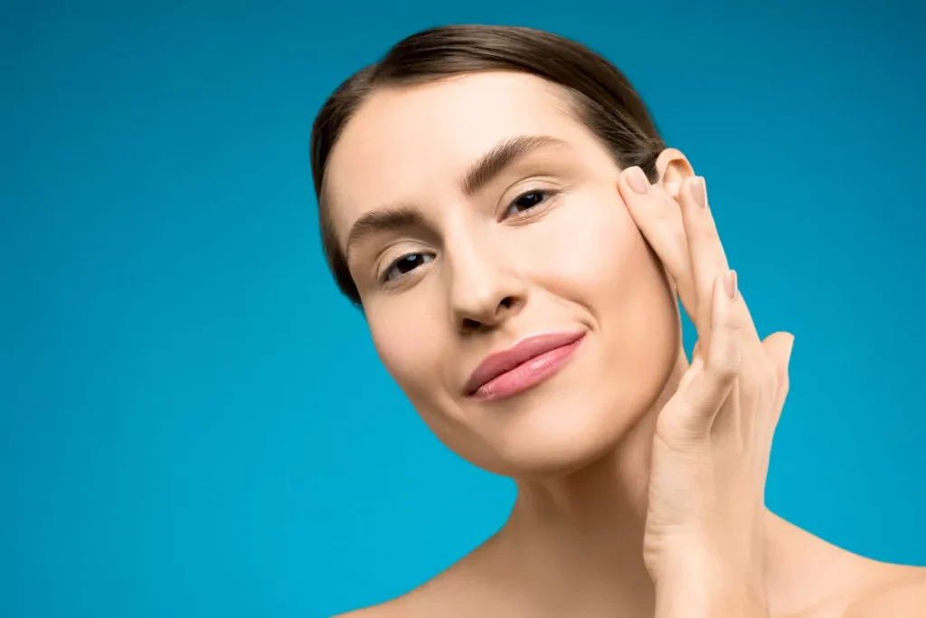 A woman touching her face, representing improved skin clarity and glow from glutathione injections