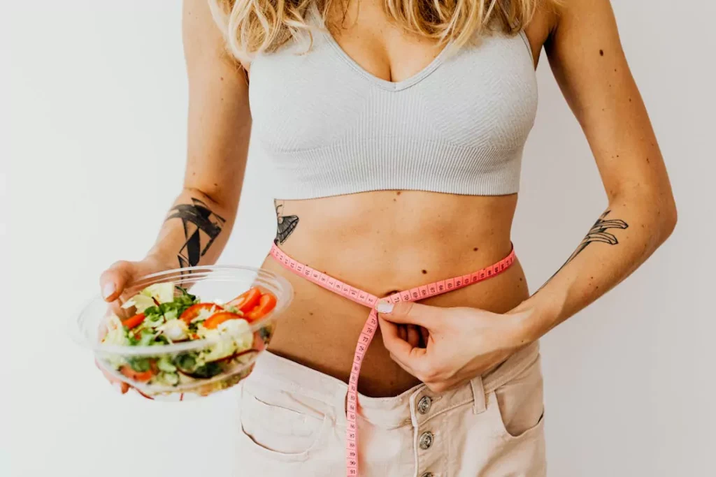 A woman measuring her waist while holding a healthy meal, representing weight management supported by semaglutide and lifestyle changes