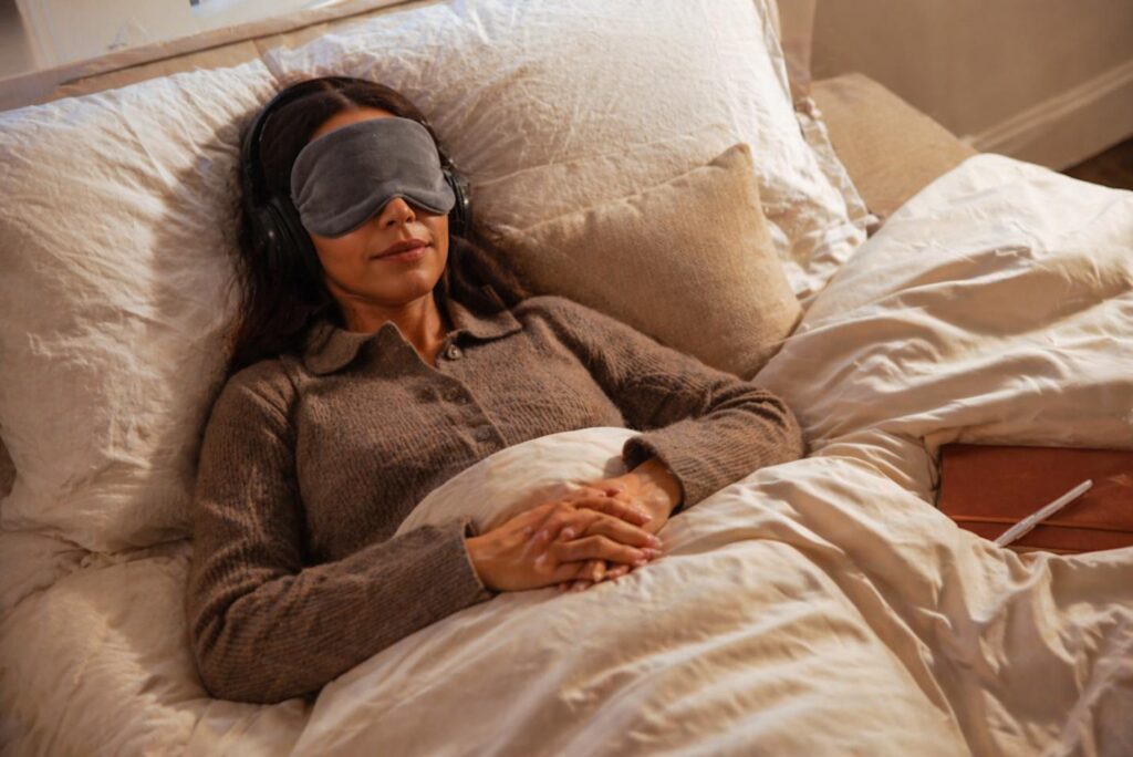 A person resting in bed with sleep mask and headphones 
