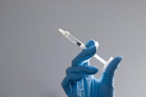 An image of a person's gloved hand holding a syringe