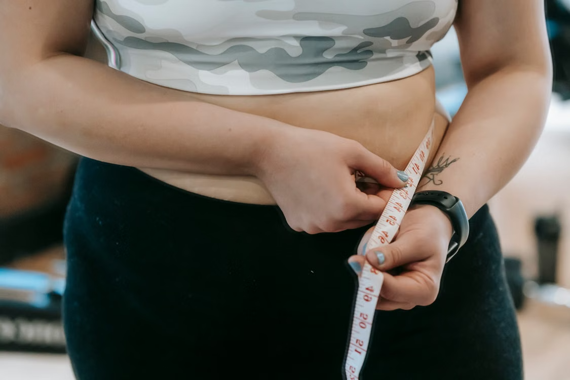 woman measuring her waist representing the connection between hormones, metabolism, weight gain, and body composition