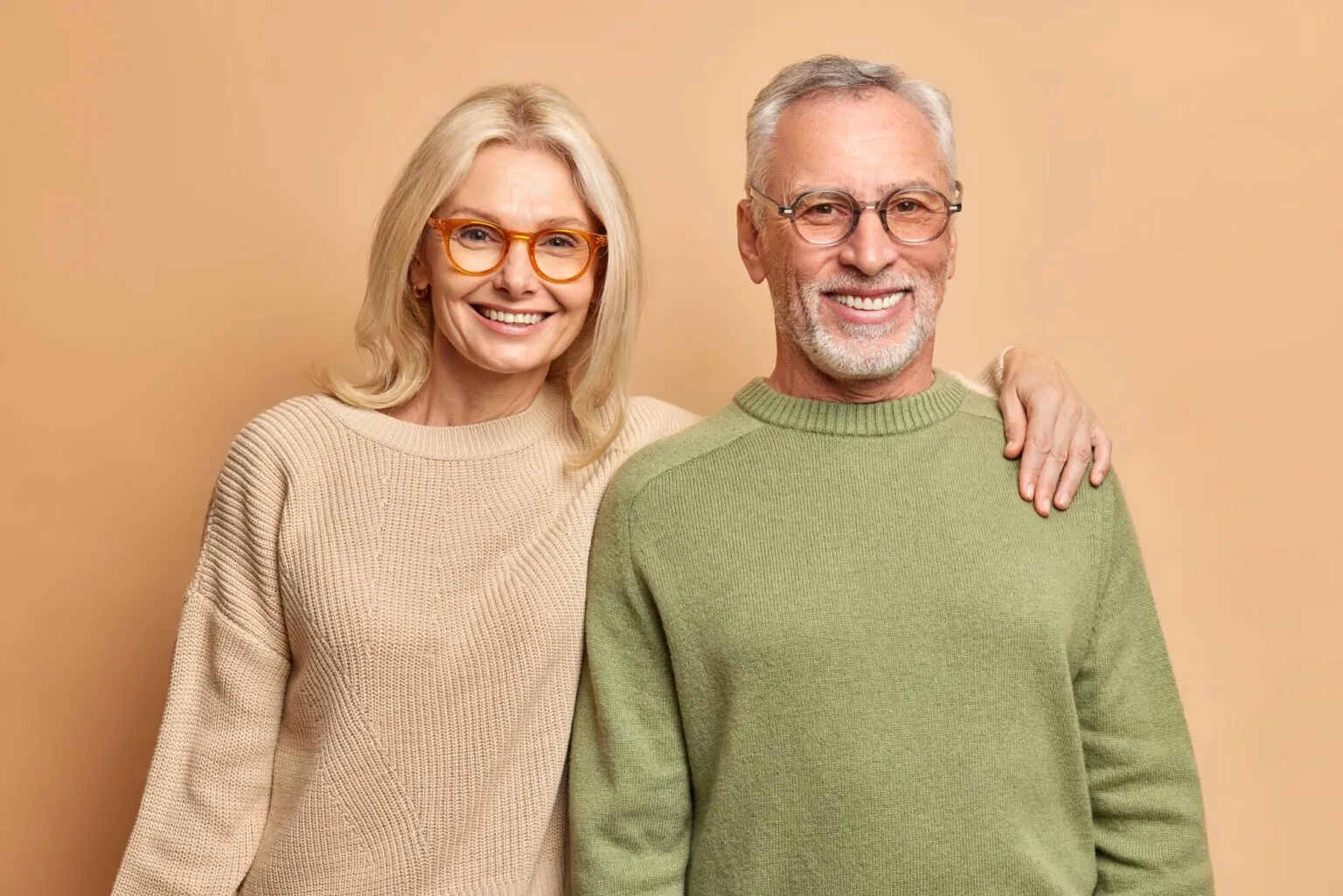 Happy mature couple smiling and standing together against a warm beige background, radiating confidence and joy.