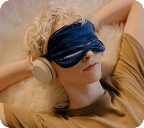 Person relaxing with headphones and a sleep mask, symbolizing rest, relaxation, and mindfulness. - Daytryp RX Person relaxing with headphones and a sleep mask, symbolizing rest, relaxation, and mindfulness.