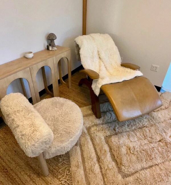 A room with a recliner and chairs covered in fluffy material, a wooden console table with a mushroom statue, and a rug.