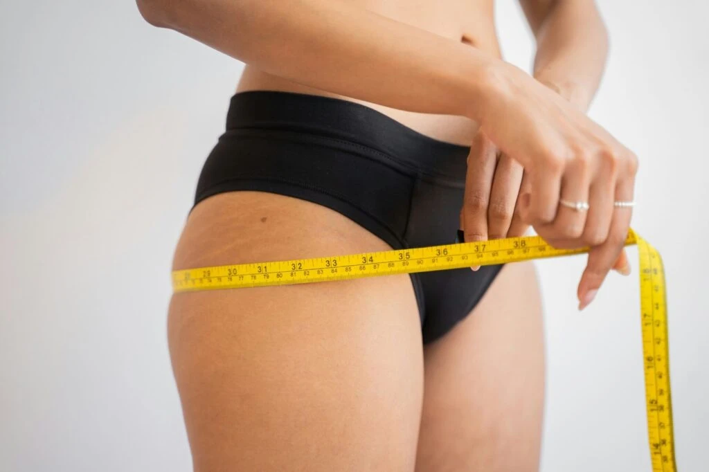 image - Daytryp RX A person wearing black underwear measures their hip with a yellow tape measure.