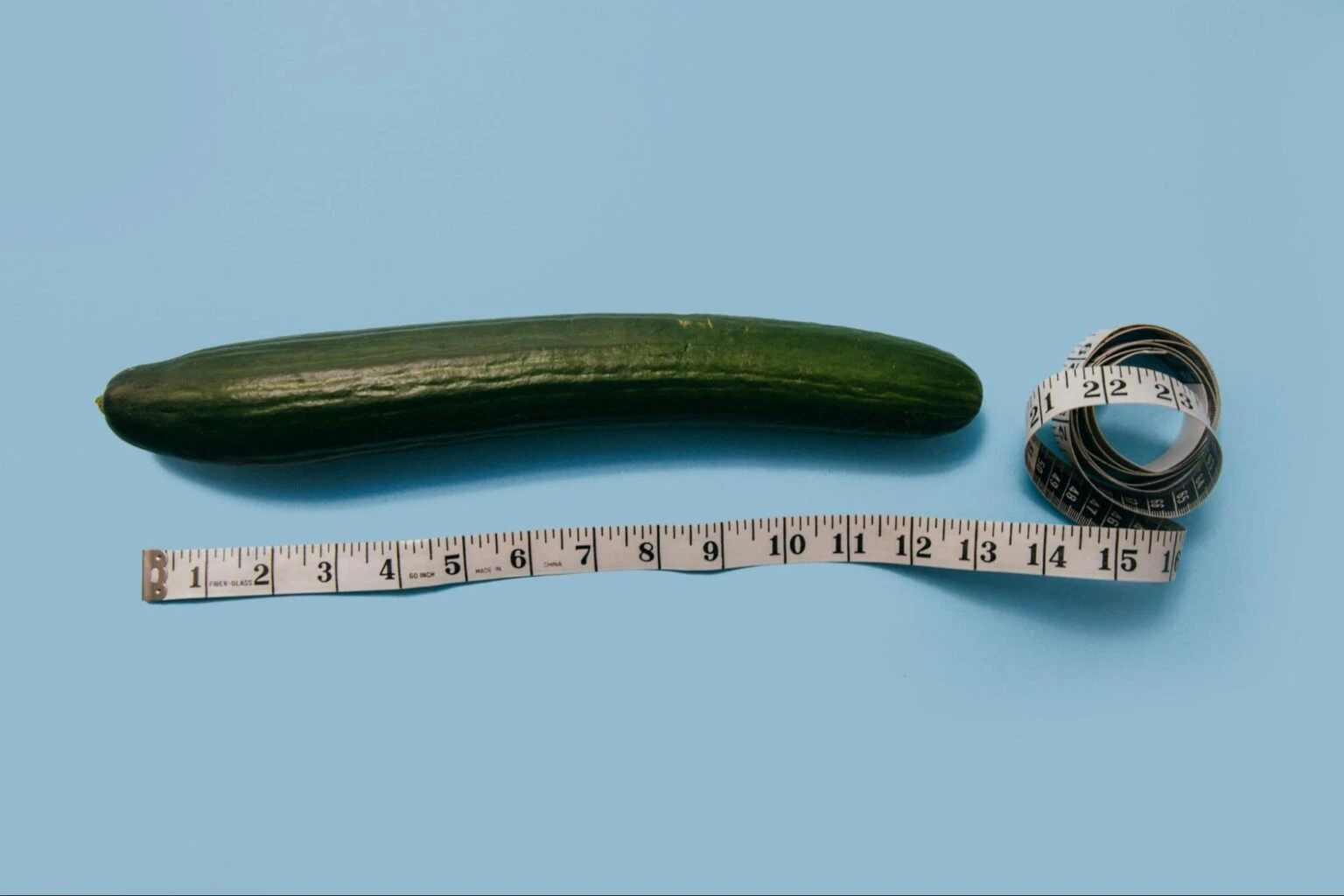 Cucumber with measuring tape symbolizing size measurement on a blue background