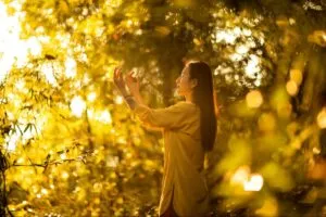 Woman practicing mindfulness or qigong in a sunlit forest during golden hour